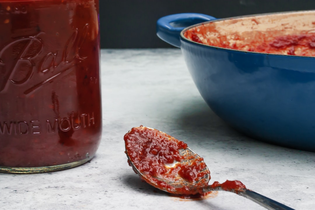 sauce on a spoon surrounded by Braiser pan and mason jar with a black background