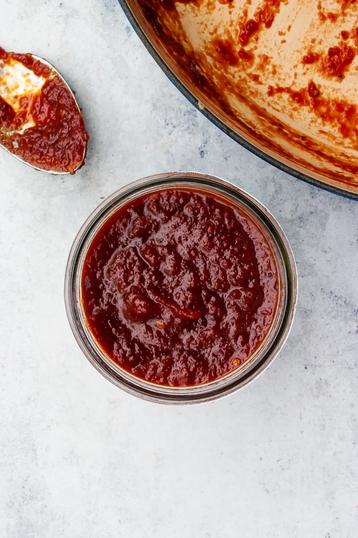 barbecue sauce in a mason jar and on a spoon with a Braiser pan in the corner