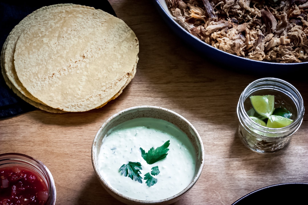 garlic-lime sauce in a bowl surrounded by pork, limes, and tortillas