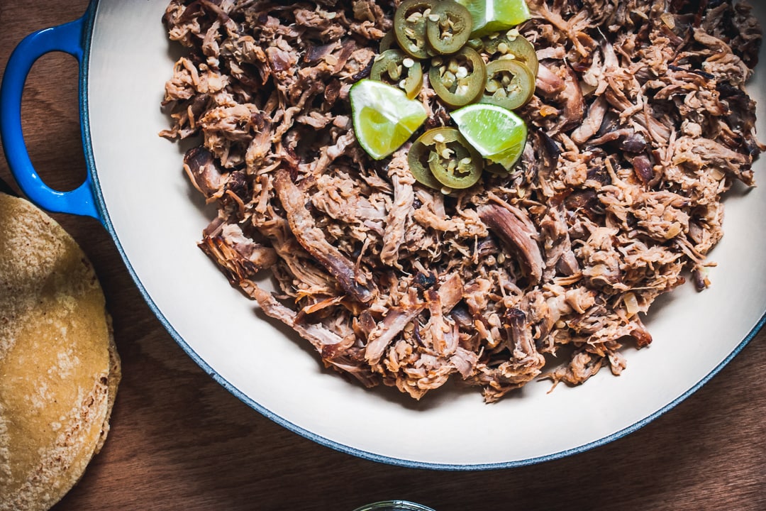 citrus pulled pork shredded in a braiser pan with limes and jalapeños on top