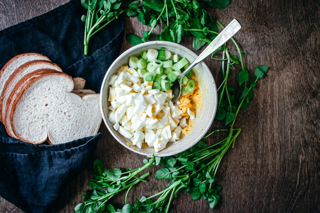 All egg salad ingredients chopped in a bowl with bread on the side