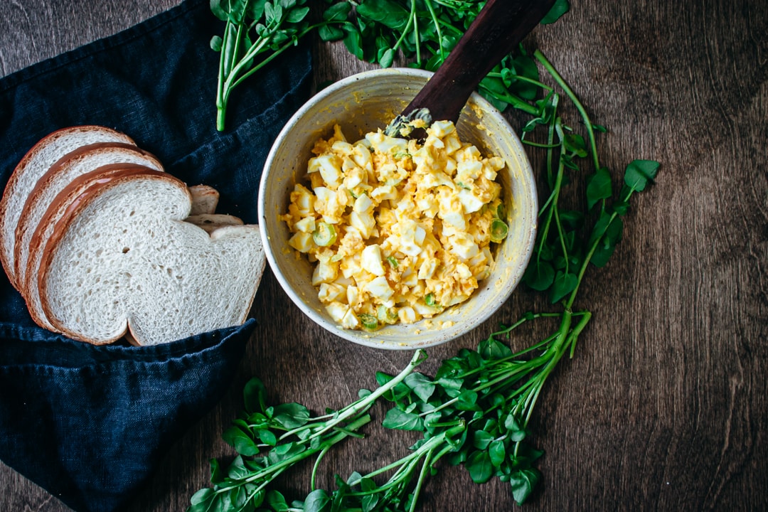 Finished egg salad in a bowl with a spreader with bread on the side