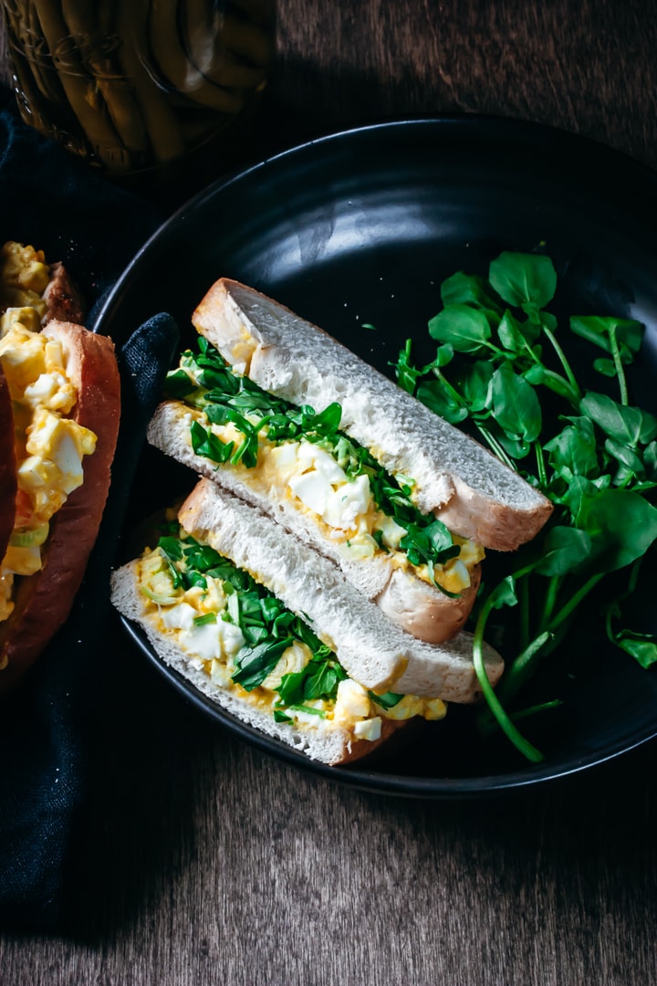 egg salad sandwich with watercress in a bowl with a second sandwich on the side