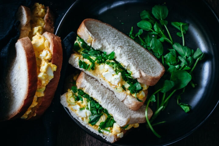 egg salad sandwich with watercress in a bowl with a second sandwich on the side