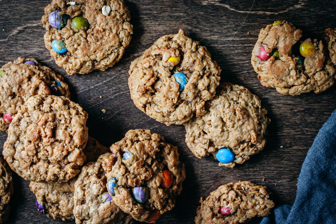 Baked Monster Cookies layered together on a dark wood background