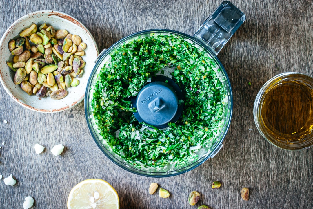 ramps, pistachios, and cheeses blended in a food processor bowl with olive oil and lemons on the side