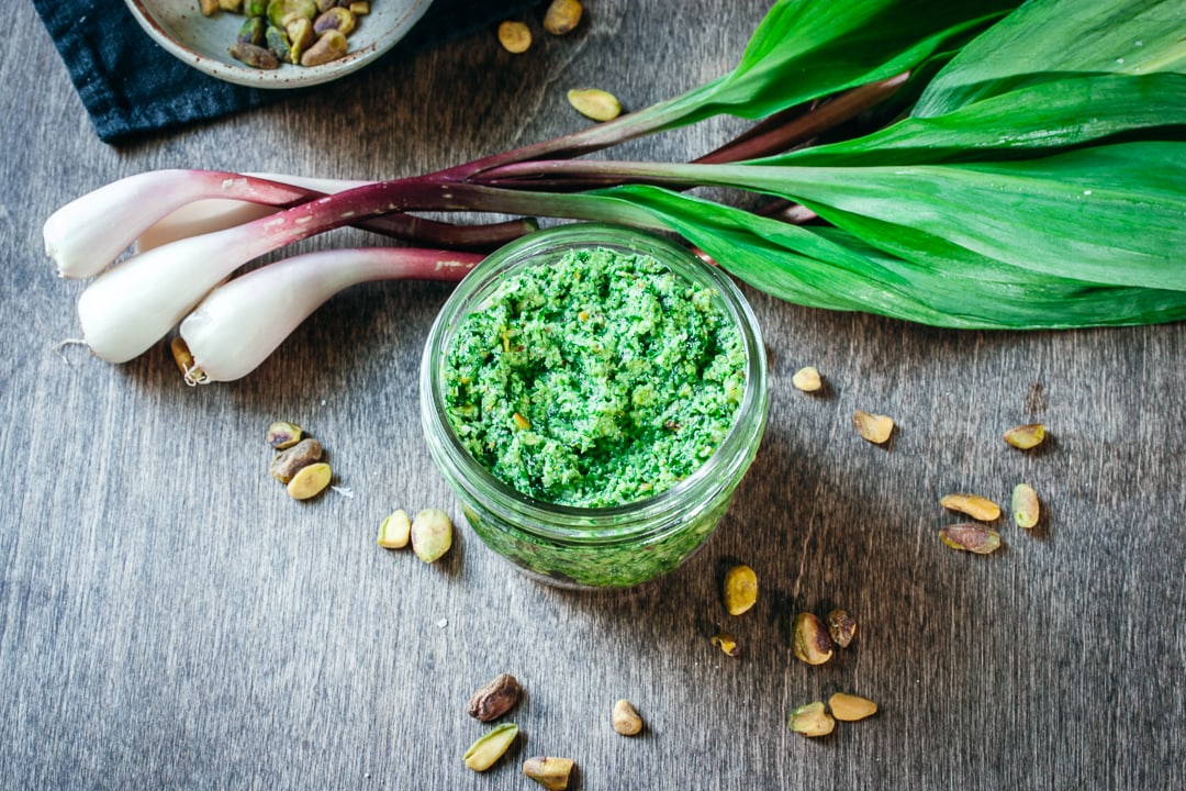 ramp pesto in a glass bowl surrounded by pistachios and ramps