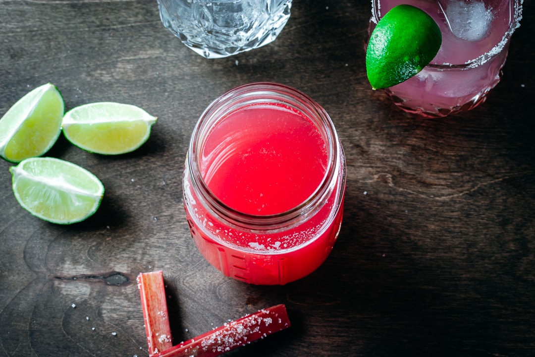 rhubarb syrup in a mason jar with rhubarb, limes, and tequila on the side