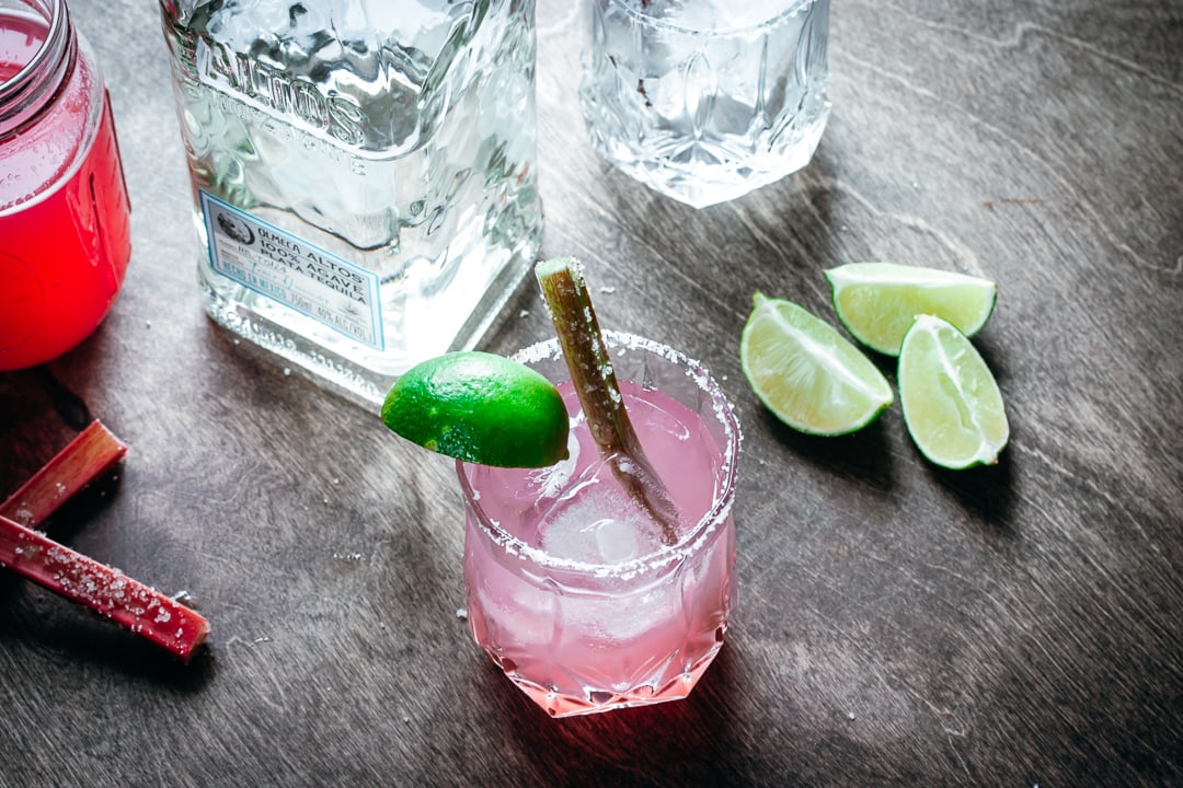 A Rhubarb Margarita with tequila, limes, and a glass filled with ice on the side