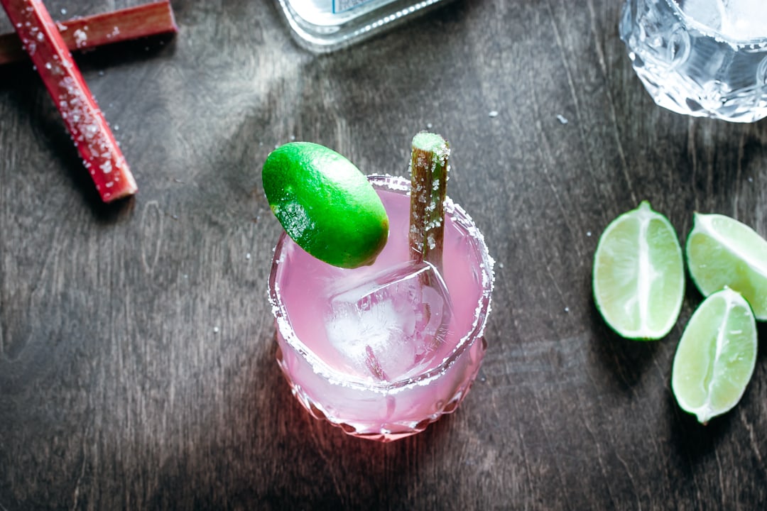 A Rhubarb Margarita with tequila, limes, and a glass filled with ice on the side