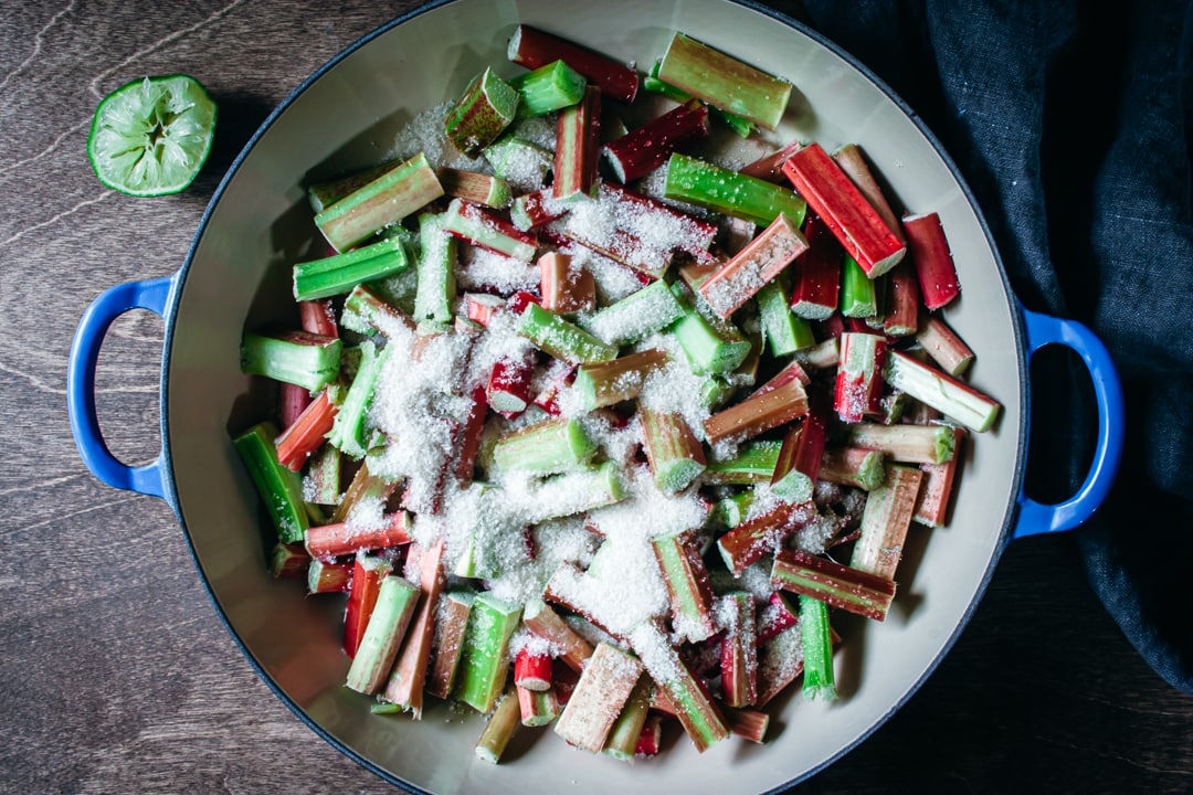 rhubarb covered in sugar in a saucepan with a lime one the side