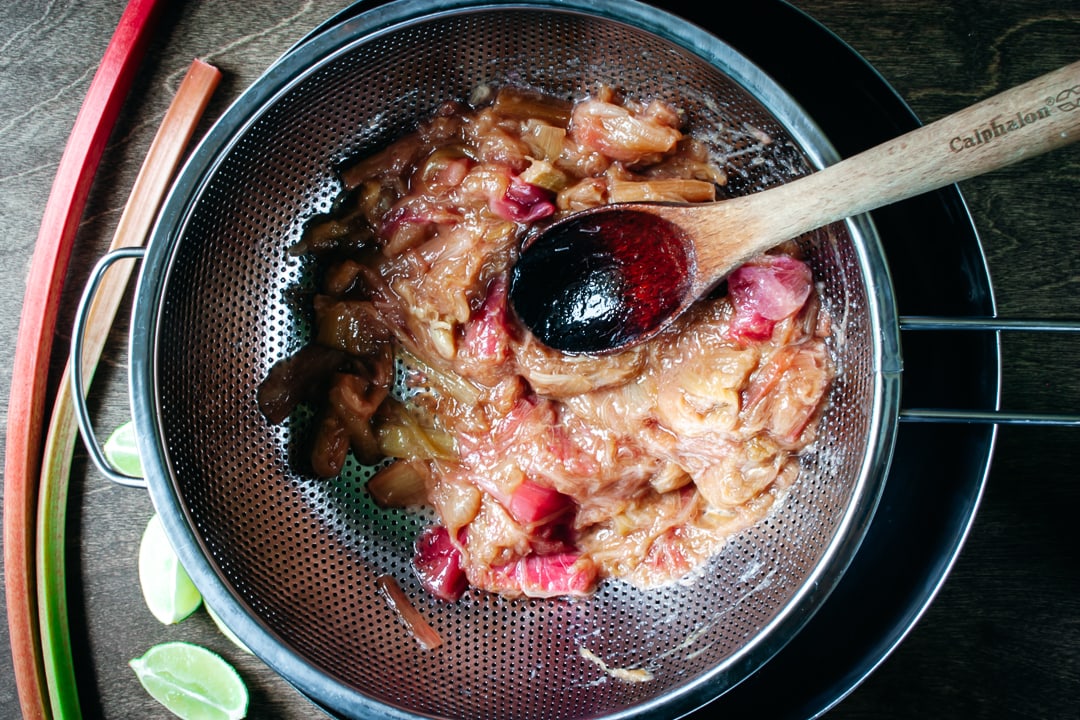 spoon pressing on the rhubarb in the strainer