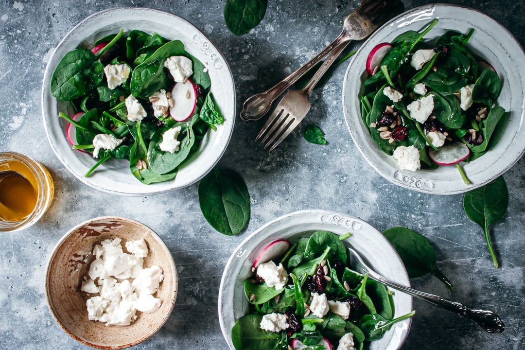 Salad in 3 white bowls with goat cheese and forks on the side