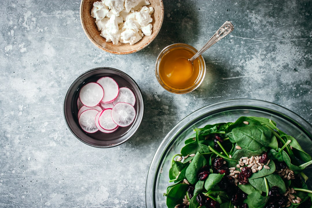 undressed salad with radishes, dressing, and goat cheese on the side