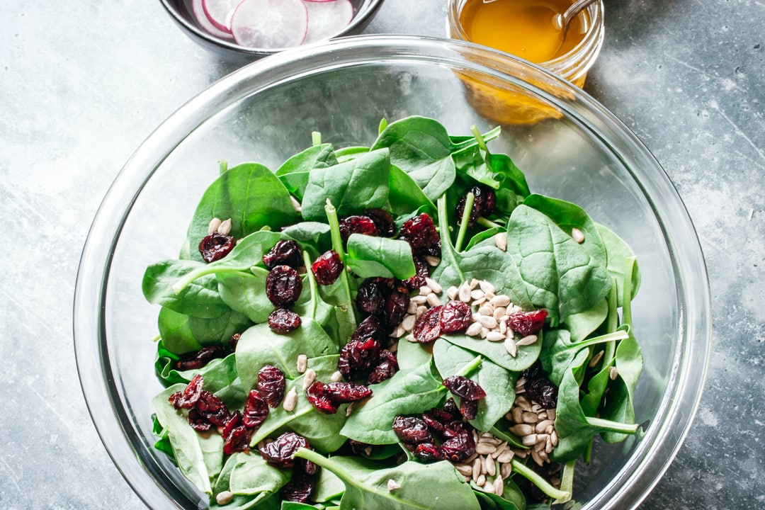 spinach, cranberries, and sunflower seeds in a glass bowl