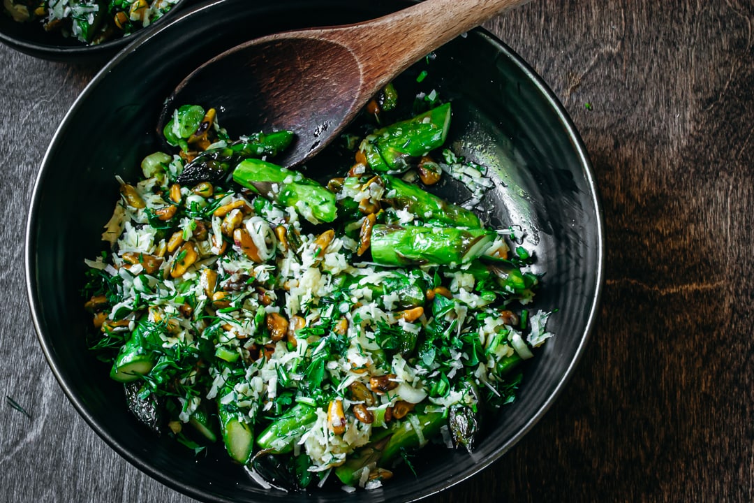 Finished Stove Top Asparagus with pistachios and herbs in a black serving bowl with a spoon