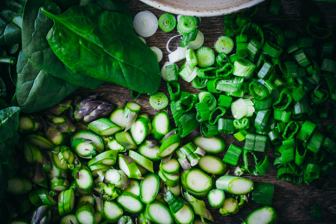 cut up asparagus, spring onions, and whole spinach leaves on a wood background