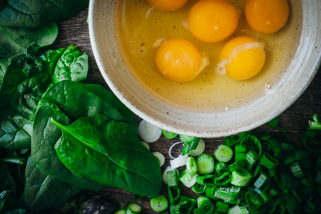 6 eggs in a bowl with spring onions and spinach on the side