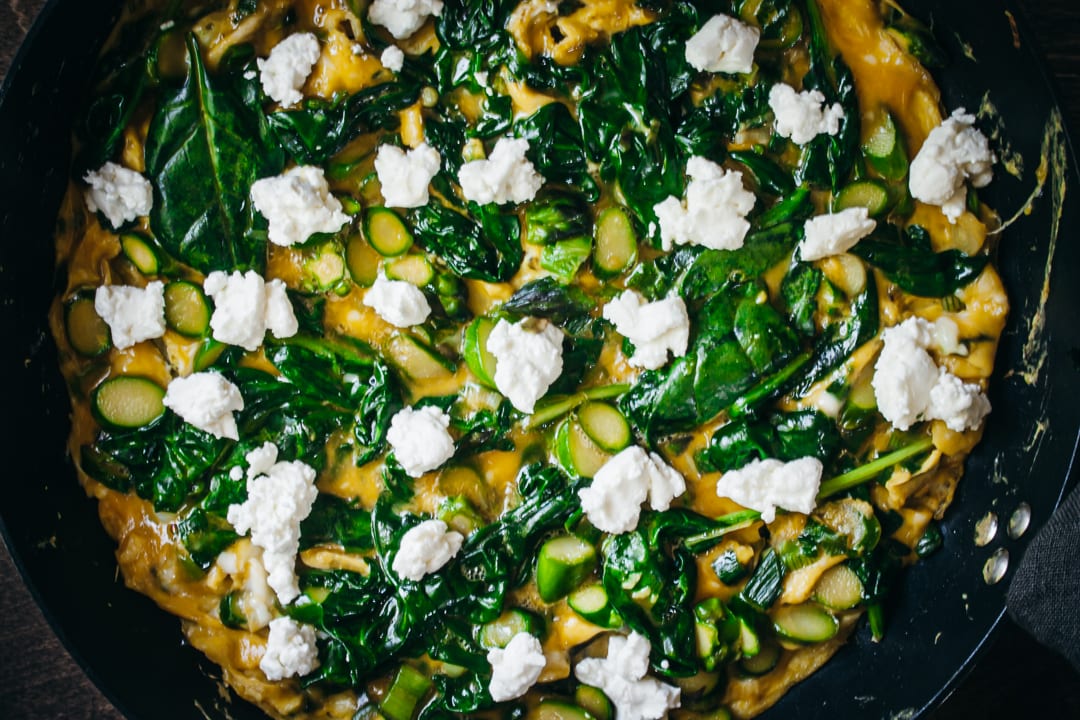 partially cooked frittata topped with goat cheese in a skillet