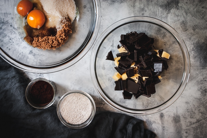 chocolate and butter in a glass bowl and sugars and eggs in a separate glass bowl