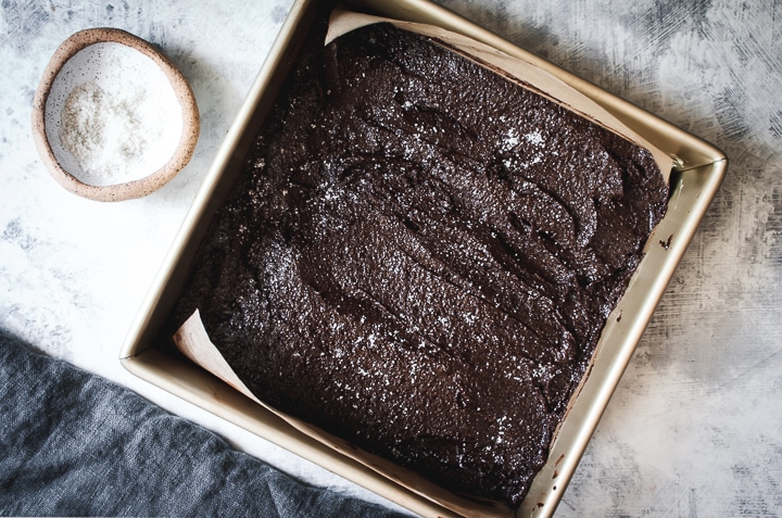 brownie batter spread in a square baking pan with salt and a napkin on the side