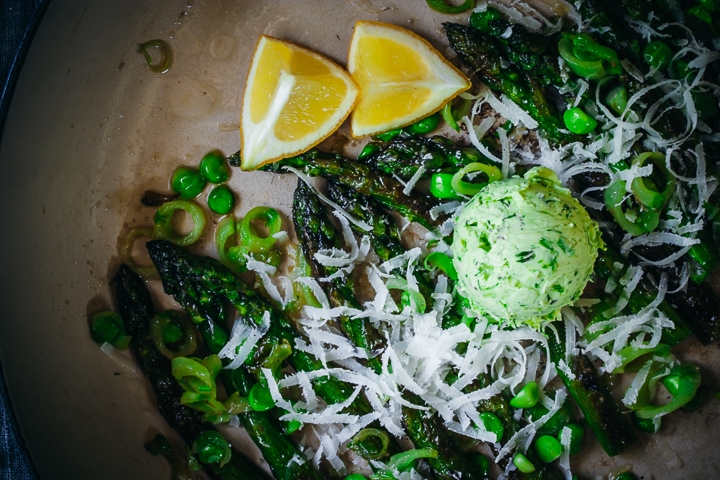 dollop of scallion compound butter on asparagus and peas with lemons on the side