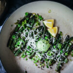 dollop of scallion compound butter on asparagus and peas with lemons on the side
