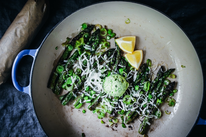 dollop of scallion compound butter on asparagus and peas with lemons on the side