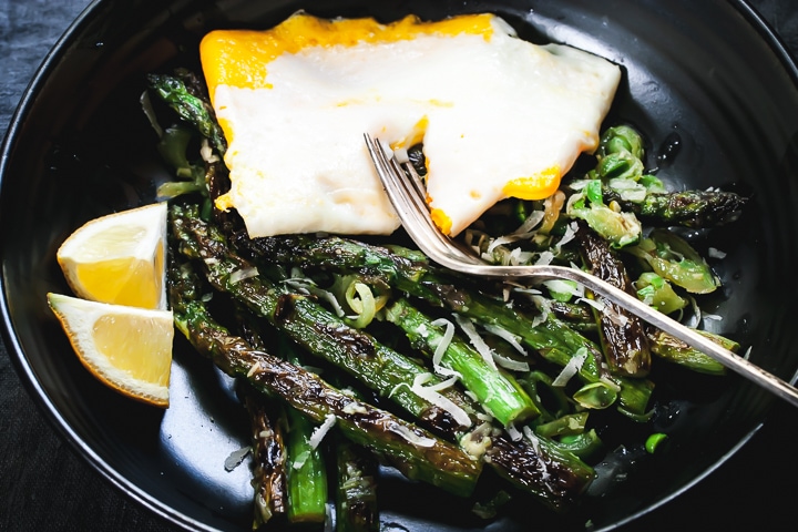 asparagus and peas topped with scallion compound butter, parmesan, and an egg with a fork