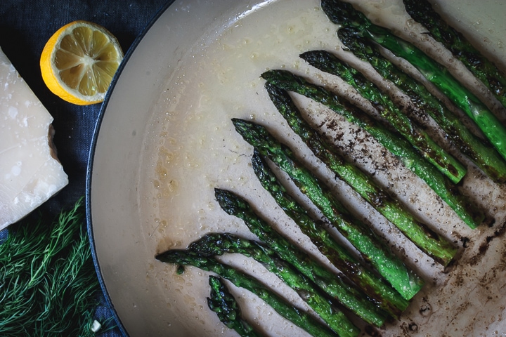 charred asparagus in a braiser pan with lemon and parmesan cheese on the side