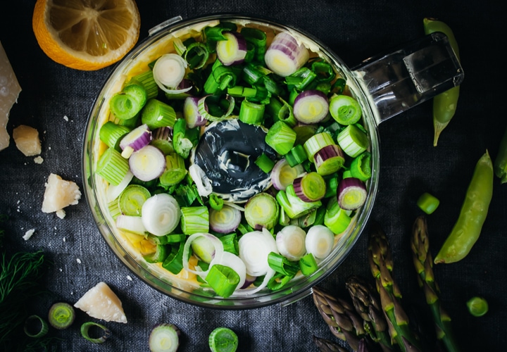 dill and scallions on top of butter in food processor bowl with chopped scallions and asparagus on the side