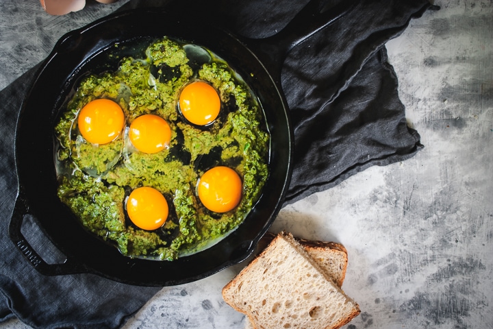 pesto spread onto the bottom of a skillet with eggs cracked on top
