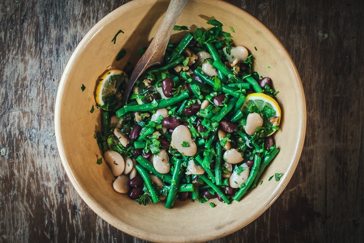 3-bean salad with lemon and dill in a yellow serving bowl with a wooden spoon