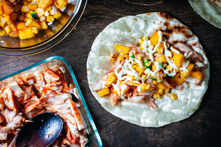 flaked fish in glass baking pan, jalapeño and peach salsa in a glass bowl, and a assembled fish taco on the side