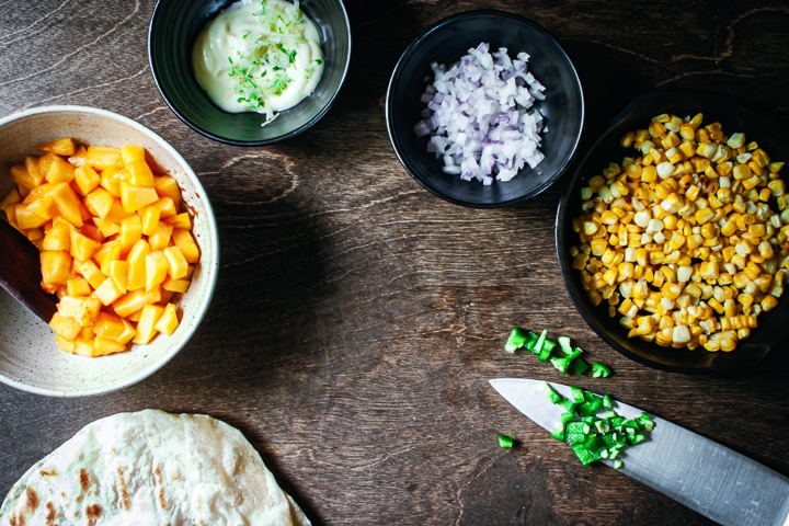 ingredients for the peach and jalapeño salsa arranged in different size bowls on a wood background