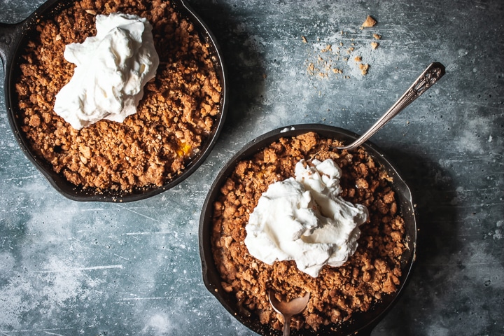 peach crumble for two in two cast iron skillets topped with whipped cream and two spoons on the side