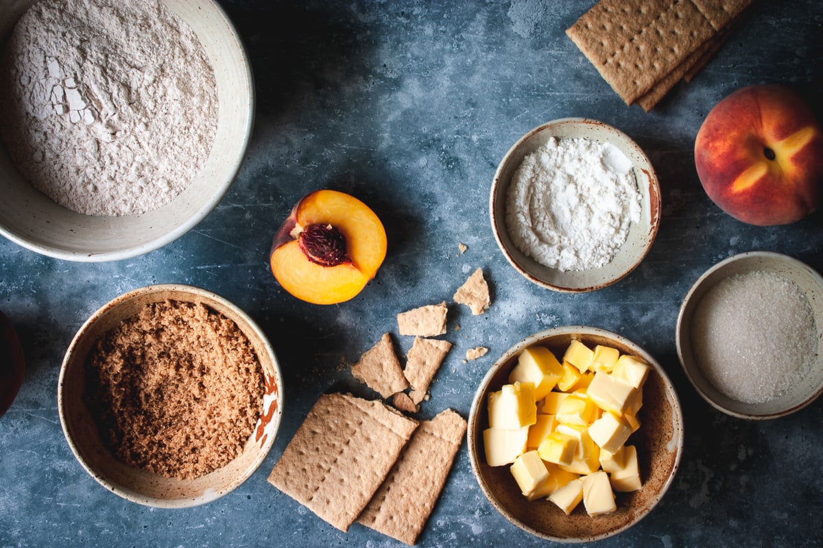 ingredients in different size white bowls with graham crackers and peaches on the side