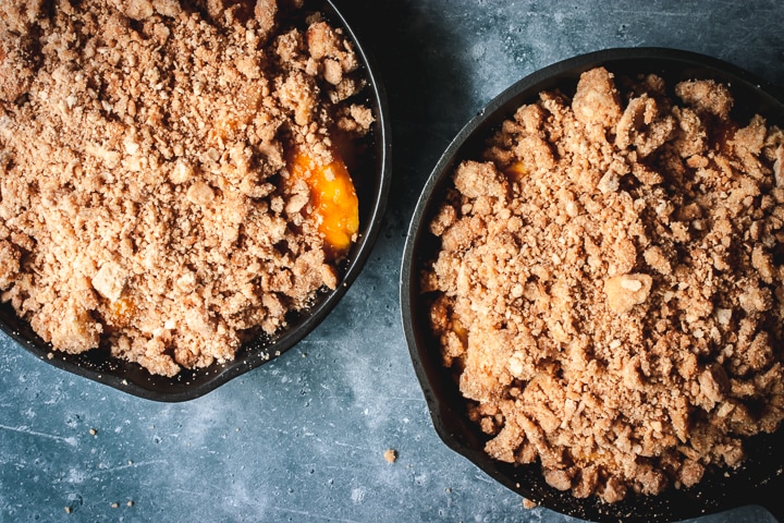 two cast iron skillets filled with peach crumble and ready to be baked