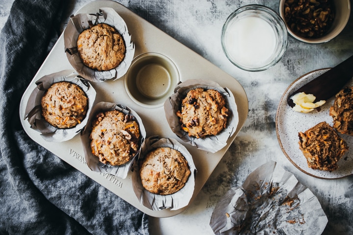 Baked whole wheat carrot muffins in a muffin tin with walnuts and milk on the side