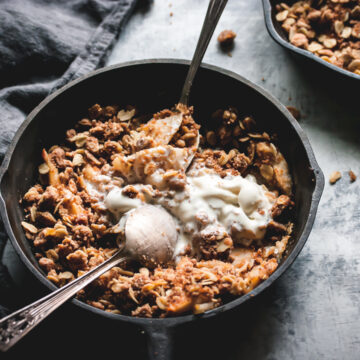 apple crisp for two with ice cream and two spoons with a napkin on the side