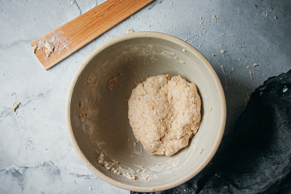 biscuit dough shaped into a ball in a bowl with a wooden spatula on the side