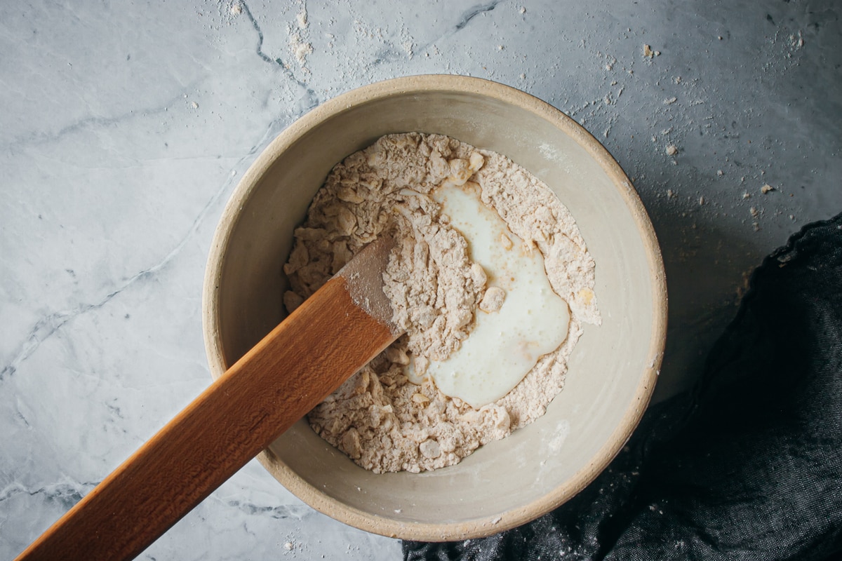 buttermilk added to dry mixture in a bowl with a wooden spatula