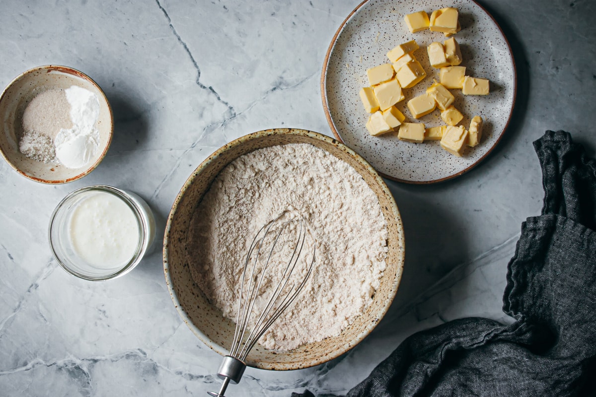 ingredients for small batch buttermilk biscuits in different size bowls and glasses with a napkin on the side