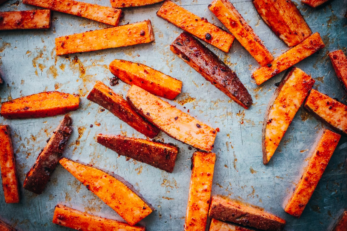 seasoned fries spread out on a baking sheet ready to be baked