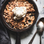 apple crisp for two topped with ice cream and two spoons on the side
