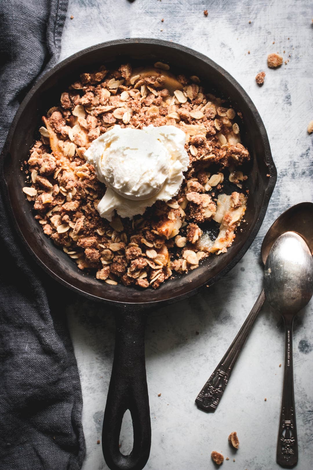 apple crisp for two topped with ice cream and two spoons on the side