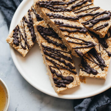 dark chocolate coconut granola bars stacked on a plate with a napkin and a bowl of honey on the side