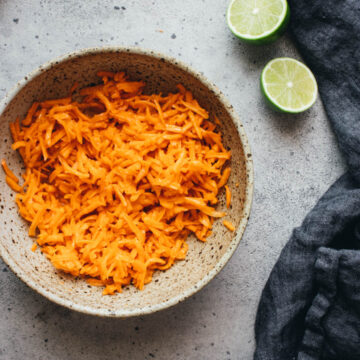 shredded carrot salad in a serving bowl with limes and a napkin on the side