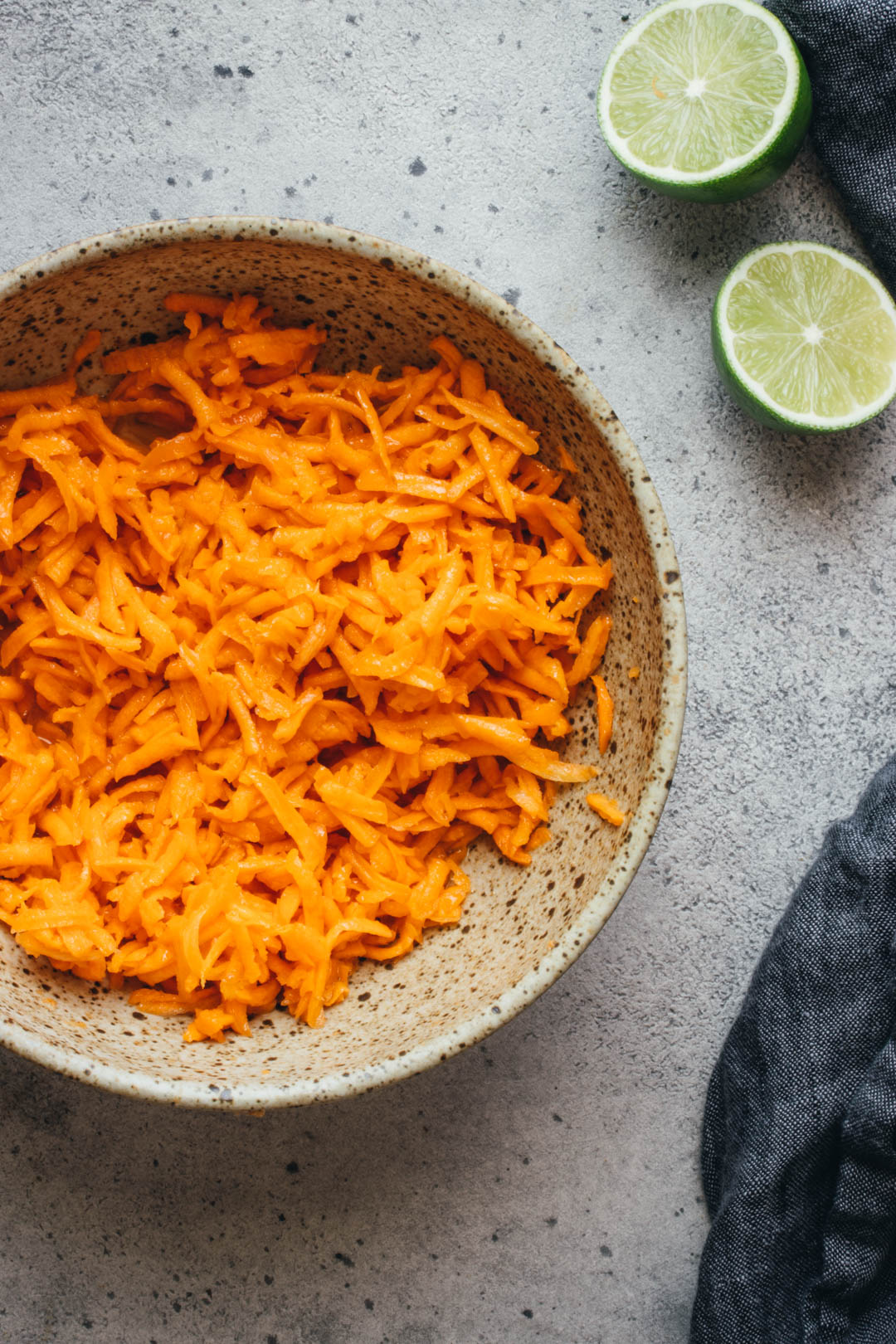 shredded carrot salad in a serving bowl with limes and a napkin on the side