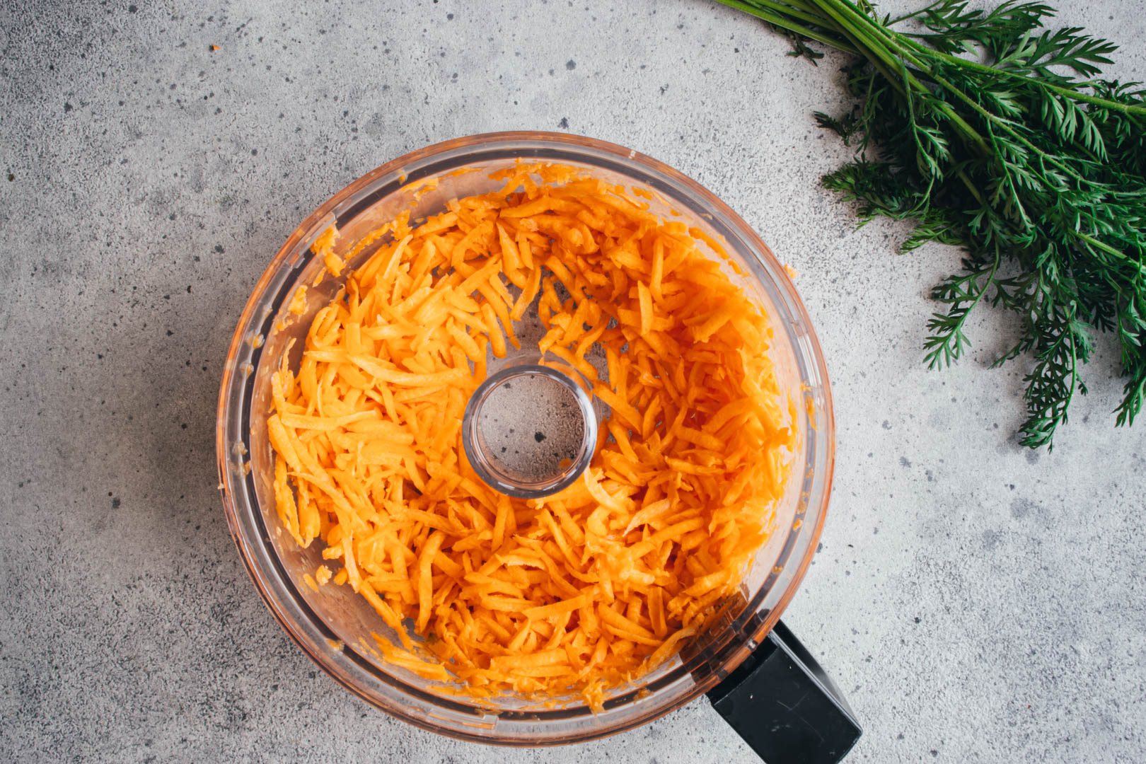 shredded carrots in a food processor with the honey lime dressing on the side